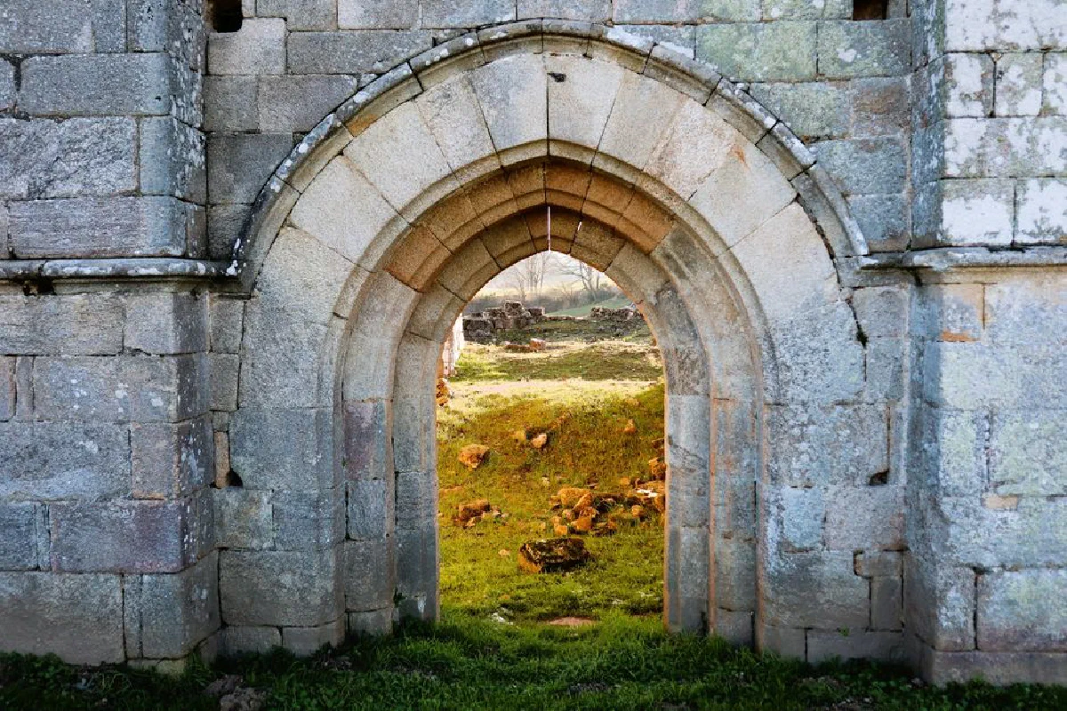 A scenic view through an ancient stone archway leading to historic ruins with lush greenery.