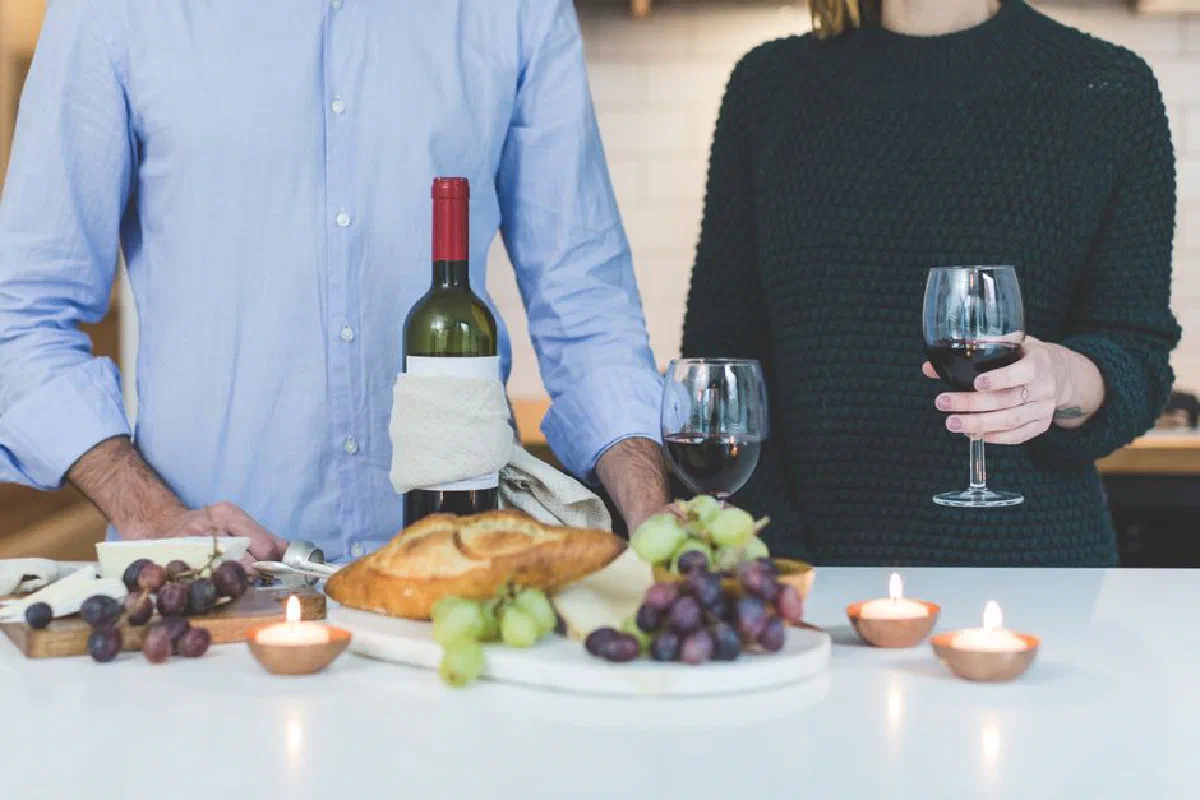 A couple shares wine and bread in a cozy indoor setting with candlelight.