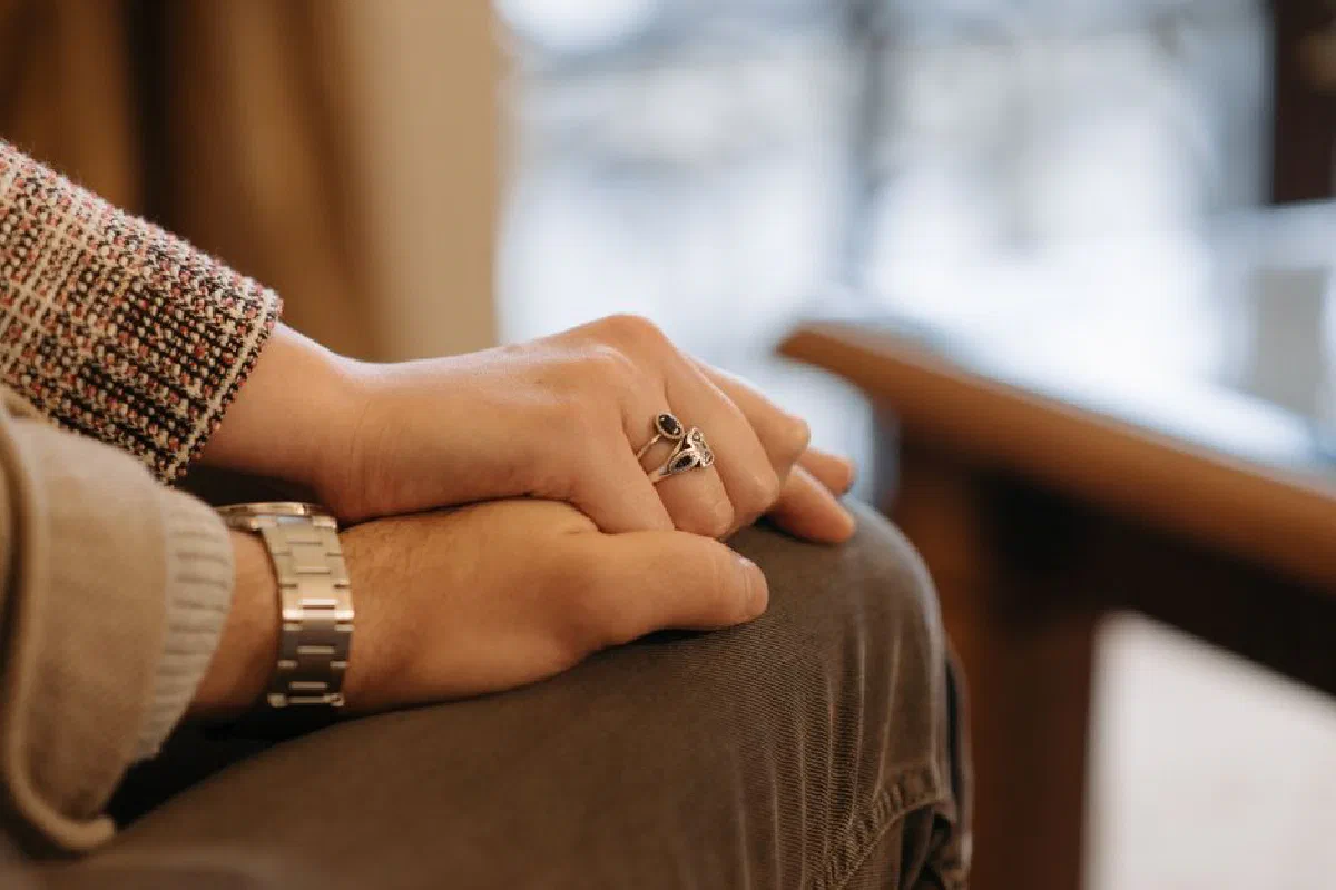 A close-up view of a couple holding hands, showcasing rings and a wristwatch, indoors.