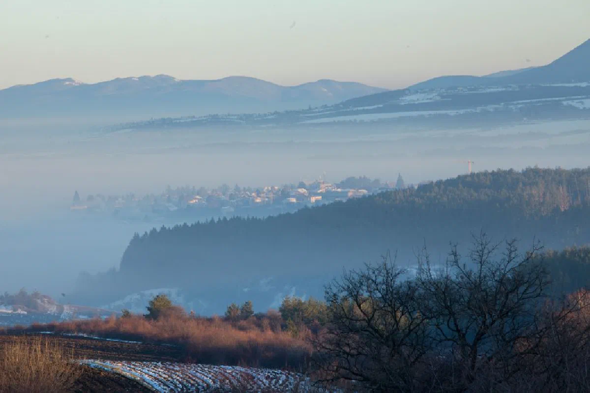 A serene misty morning view of a village nestled among rolling hills and mountains.
