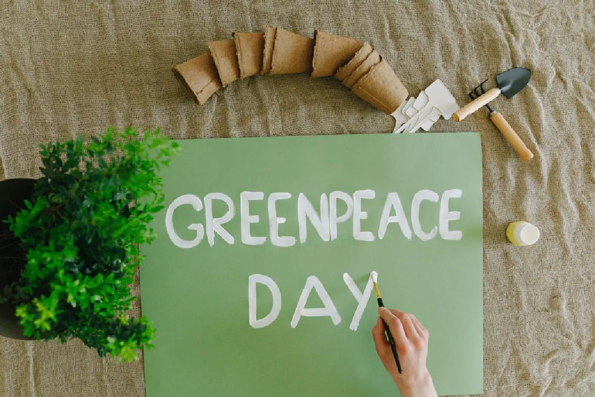 Top view of a hand painting Greenpeace Day on a green poster with gardening tools and plants.