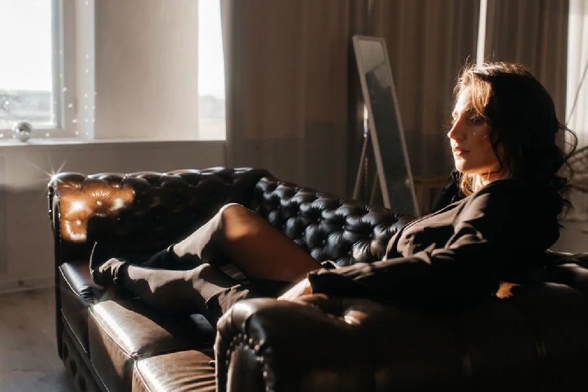 A woman relaxing on a leather sofa by a window, enjoying the sunlight in an elegant room.