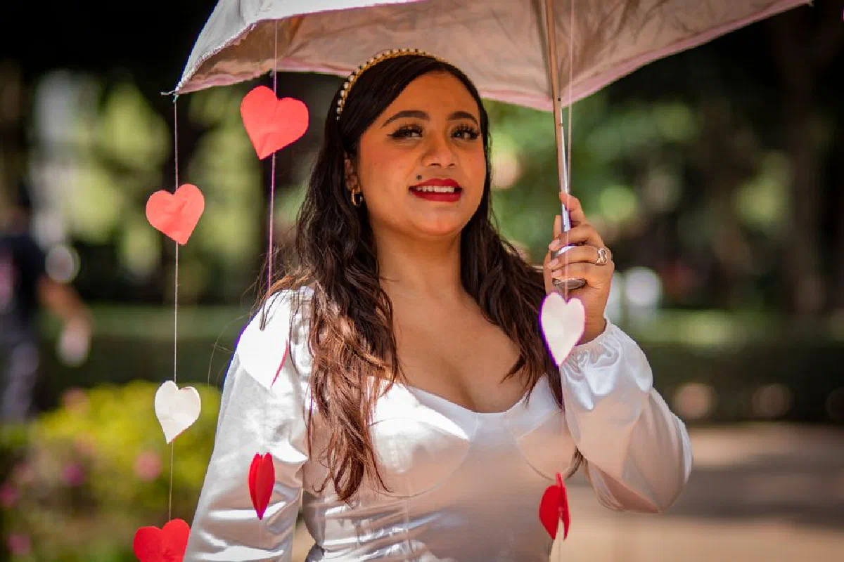 Young woman holding umbrella with heart decorations in a sunny park.