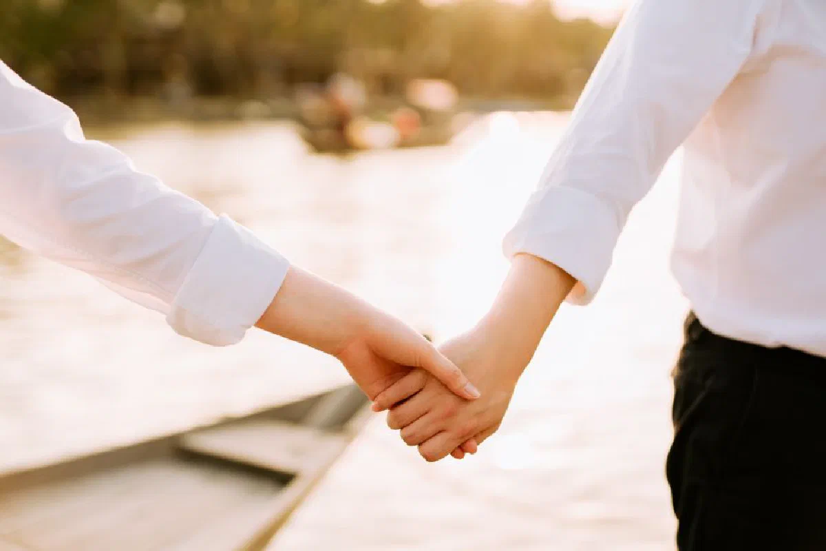 Close-up of a couple holding hands near a lake at sunset, symbolizing love and connection.