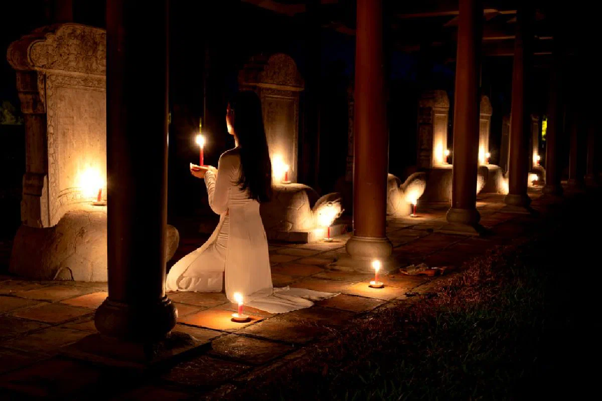 Woman in tranquil candlelight, kneeling in a temple at night, embracing spirituality.
