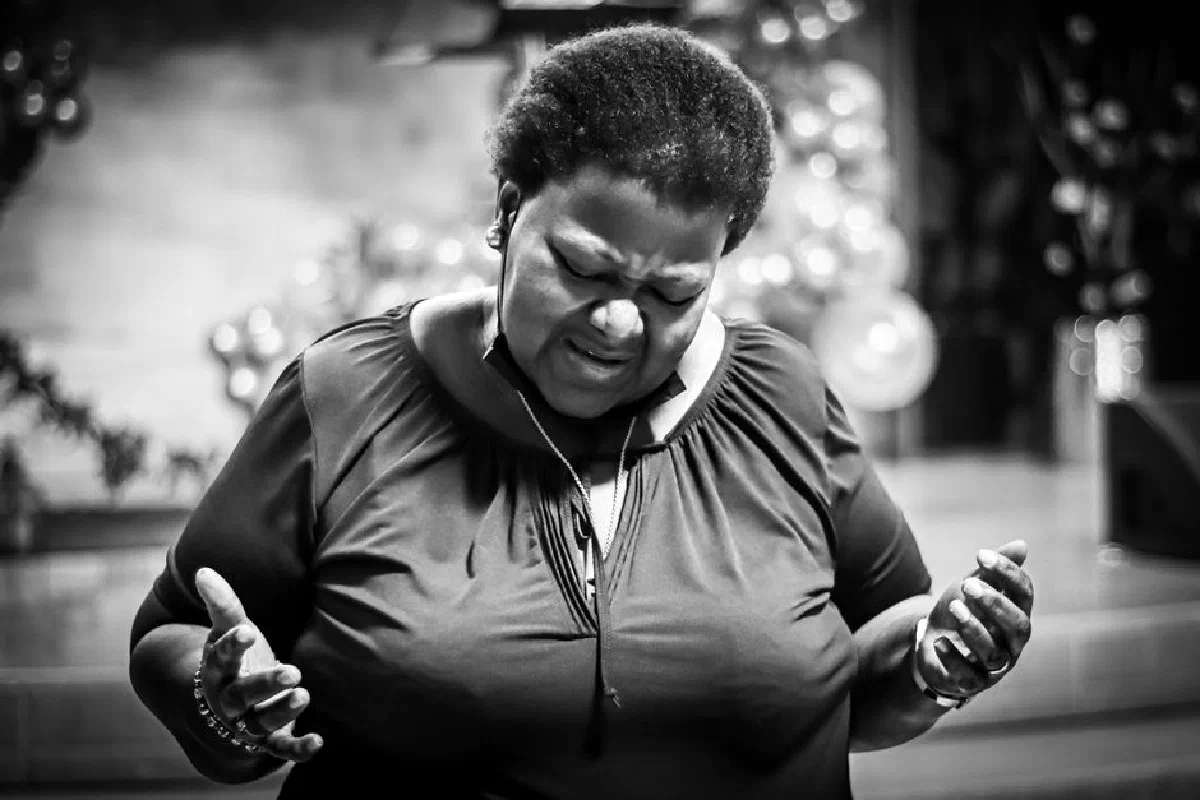 A black and white photo of a woman praying with closed eyes in a peaceful setting.