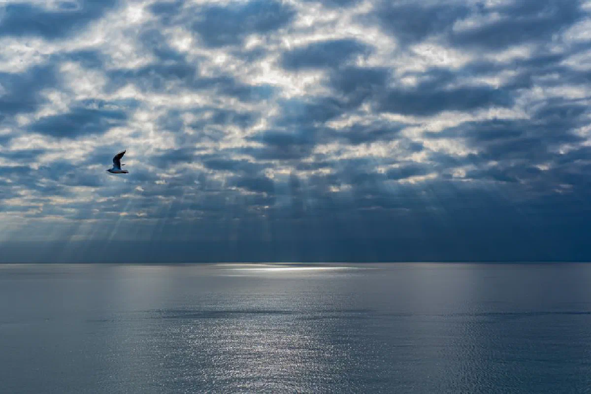 A tranquil seascape with sun rays piercing through clouds over a calm ocean.