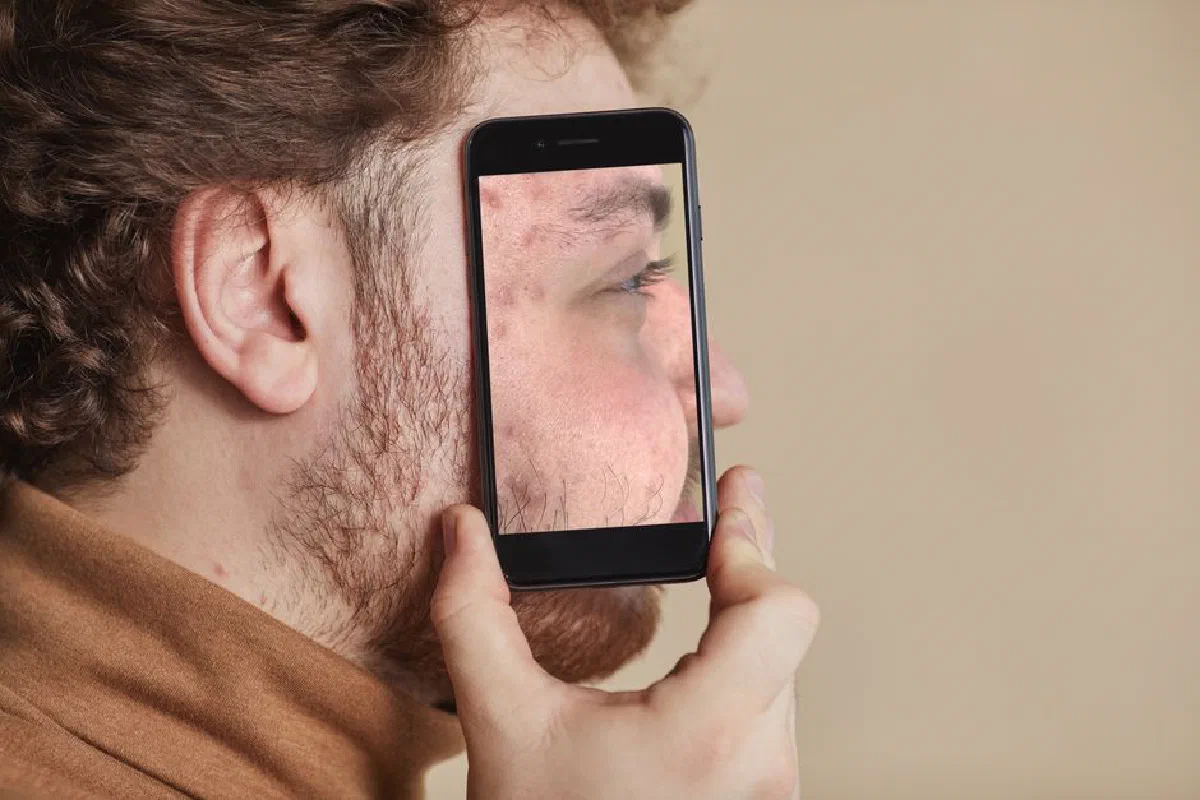 An adult man holding a smartphone displaying his facial reflection, illustrating creative mobile photography.