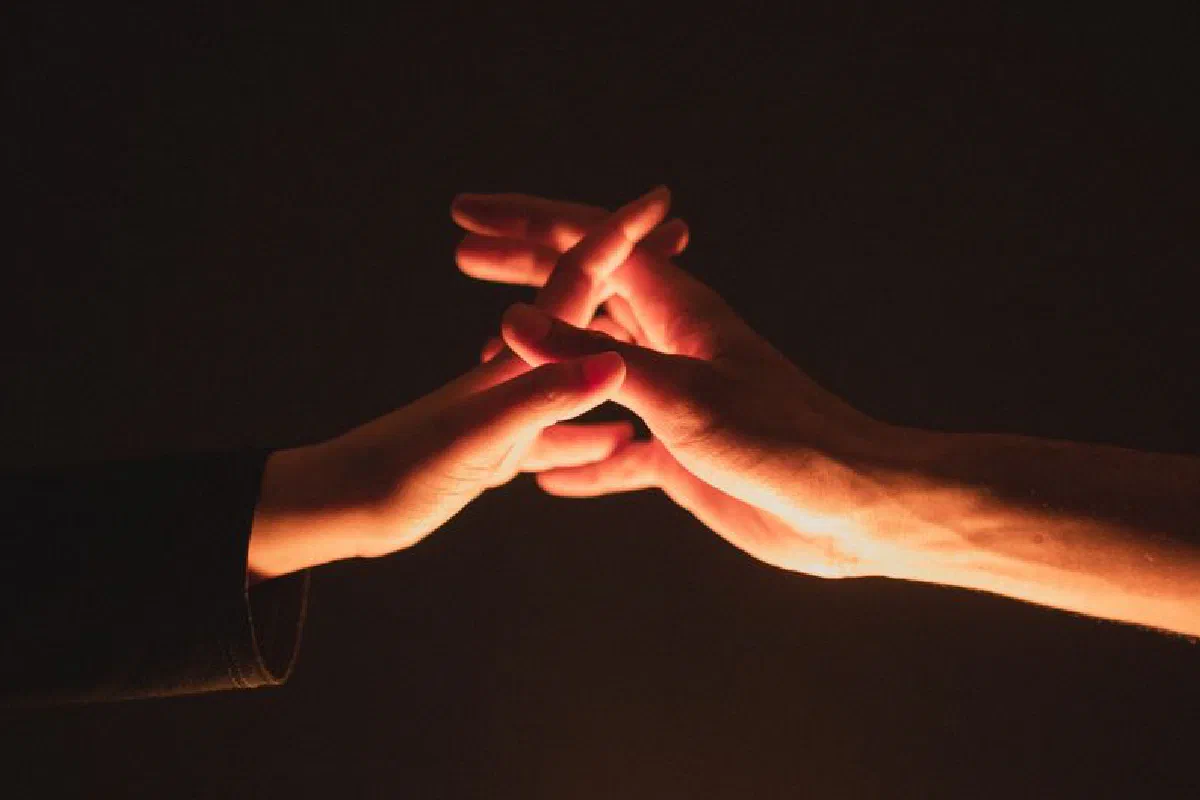 A close-up image showcasing two hands reaching towards each other in warm lighting.