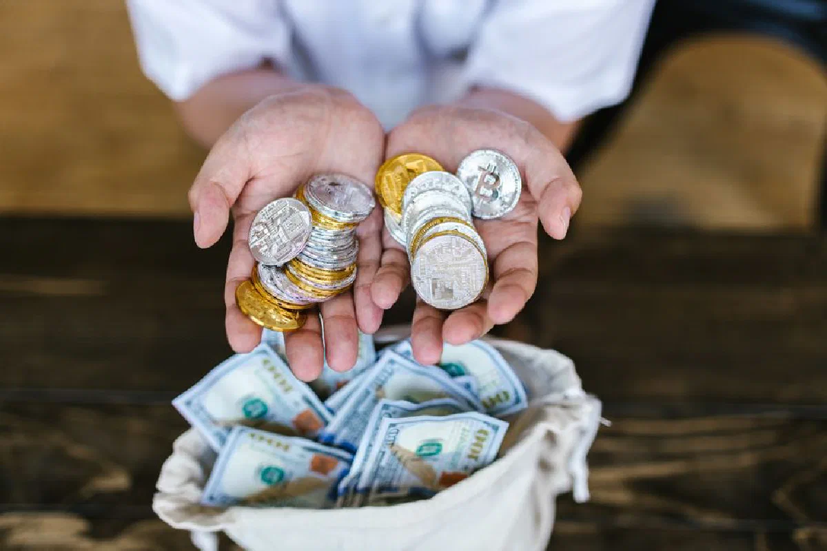 Person holding cryptocurrency coins above a bag of cash, symbolizing digital and traditional finance intersections.
