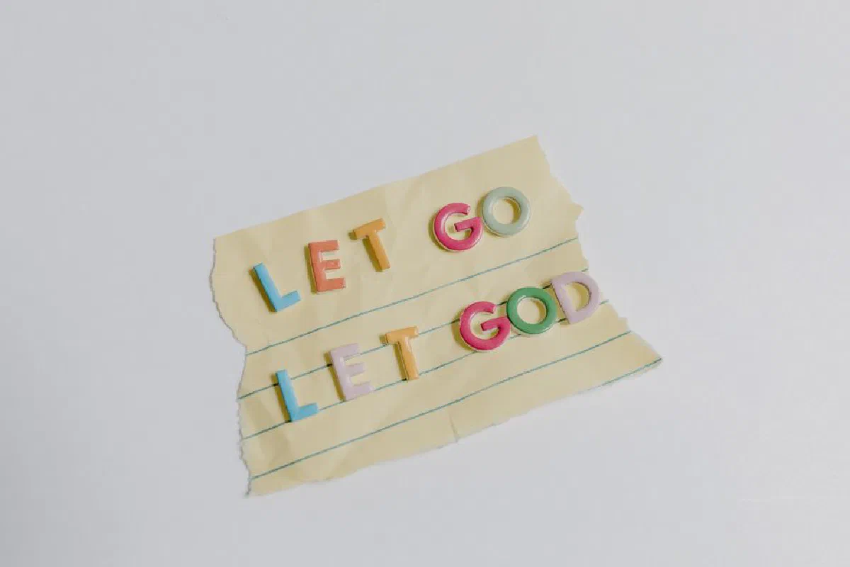 Colorful letters spell 'Let Go, Let God' on torn yellow lined paper.