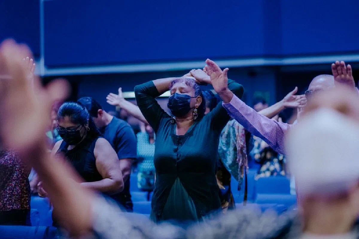 A group of people wearing masks, praying in a church setting, highlighting spirituality and safety.