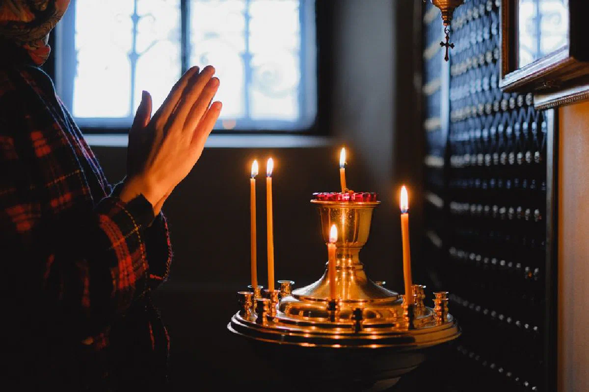 A woman in prayer beside a candelabrum in an ambient church setting.