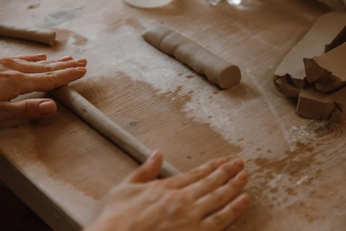Close-up of hands crafting a clay piece by rolling it on a wooden table.