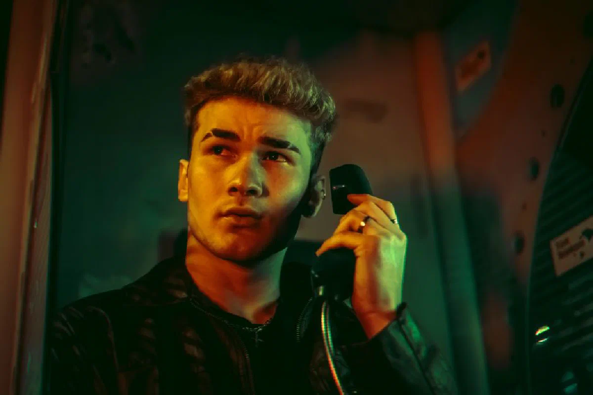 Portrait of a young man in a telephone booth holding a phone with dramatic lighting.