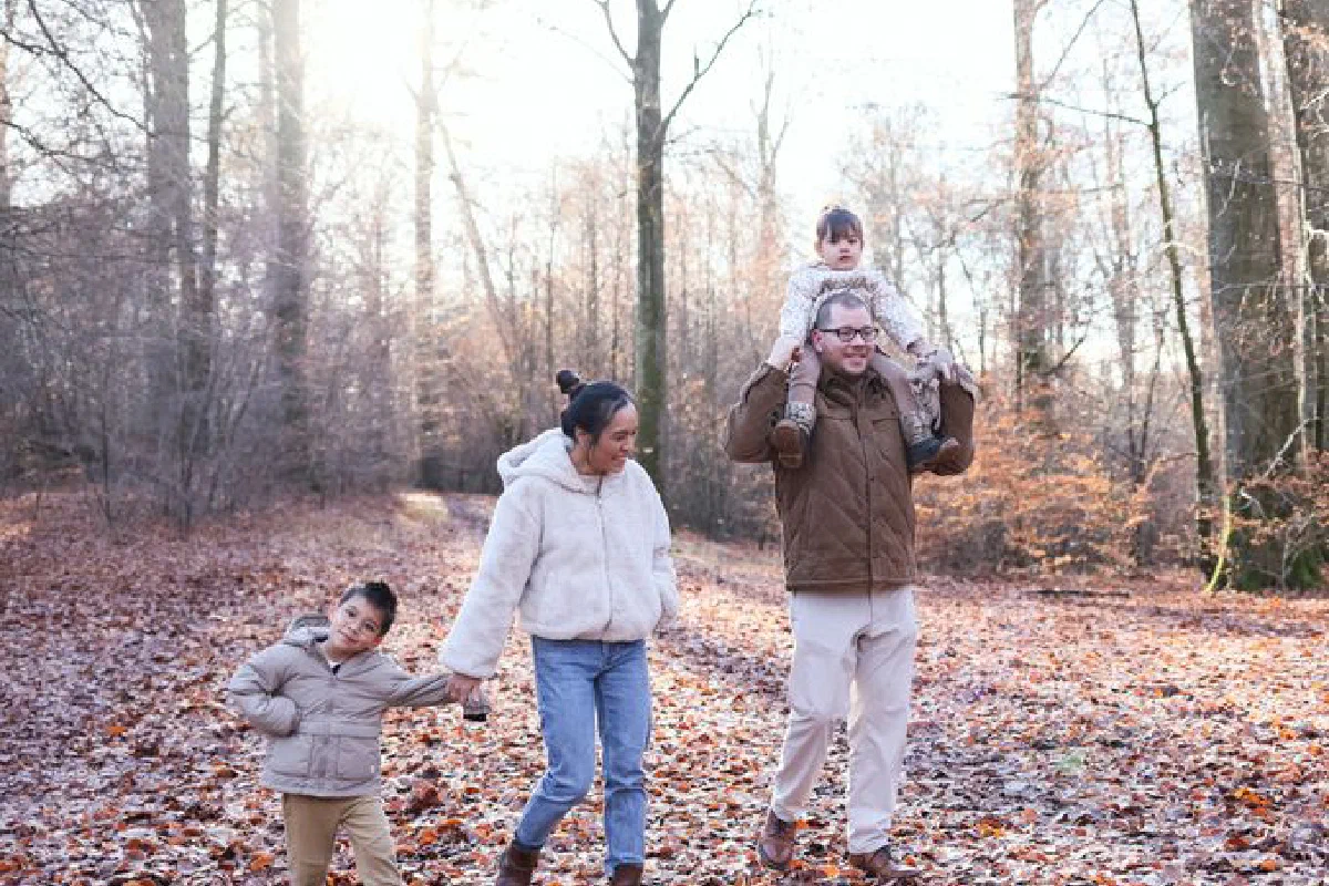 Happy family walking through a sunlit autumn forest path, enjoying quality time outdoors.