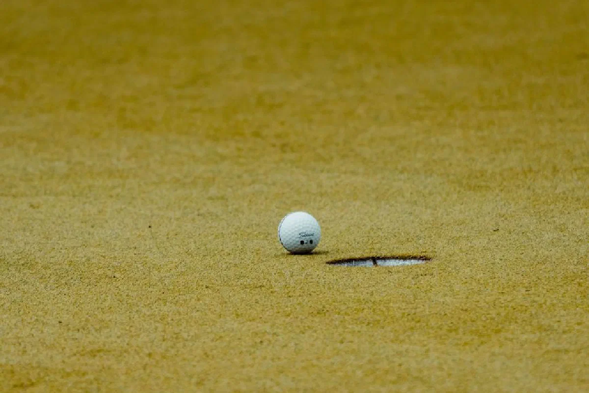 A golf ball positioned near the hole on a sandy golf course green in Türkiye, emphasizing sport precision.