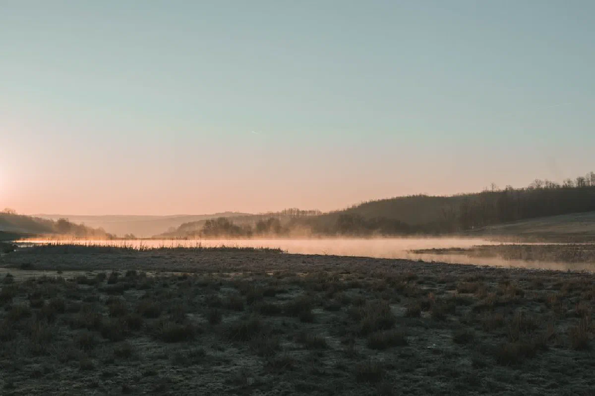 A serene winter sunrise with mist over a river in Romania, capturing the tranquil beauty of nature.