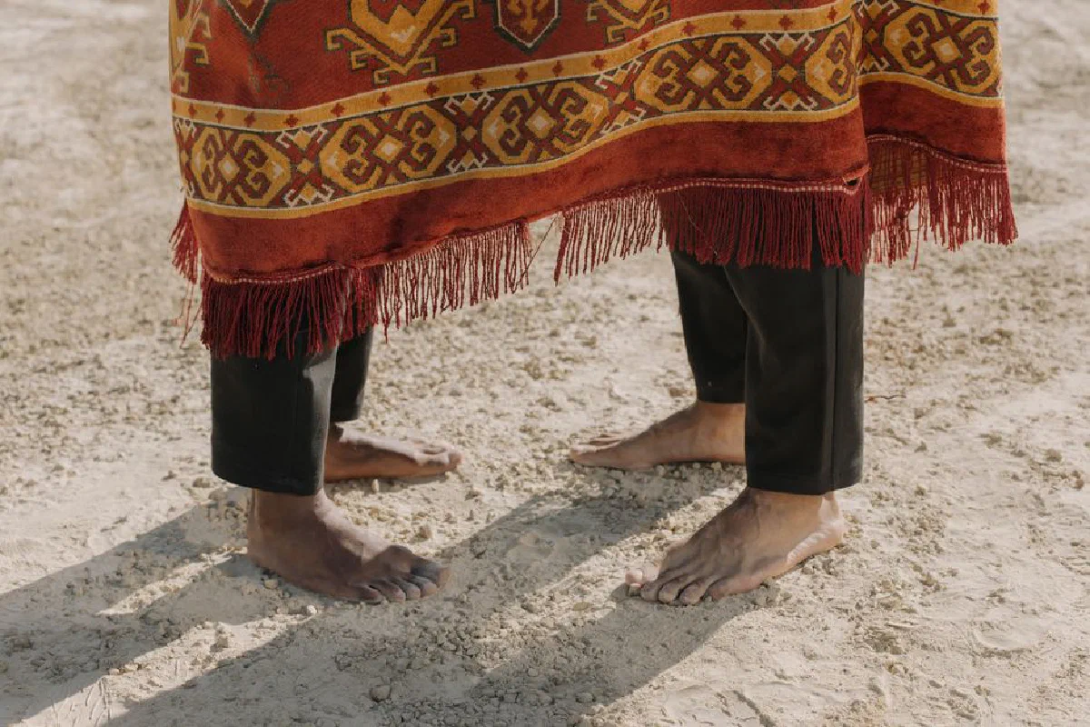 Close-up of feet on sandy ground, draped in a woven textile, representing cultural elements.