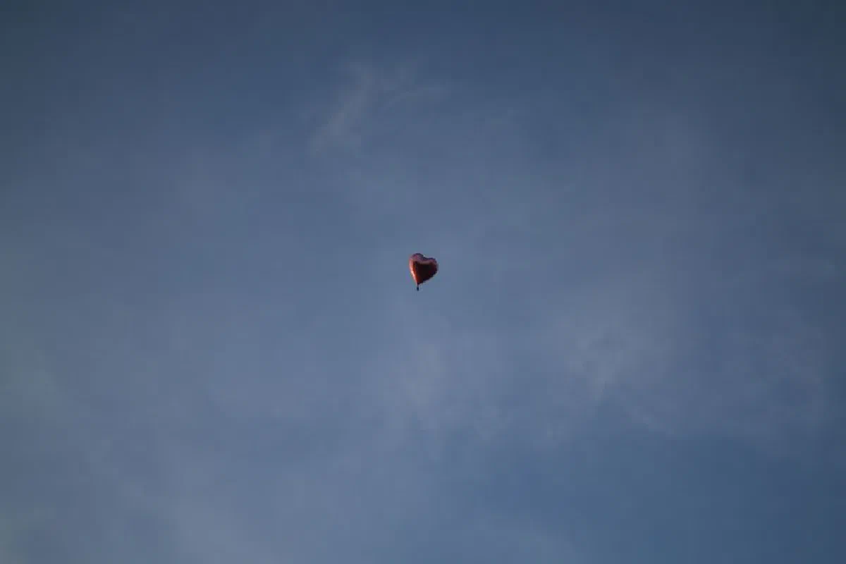 A single heart-shaped balloon floats freely against a serene blue sky.