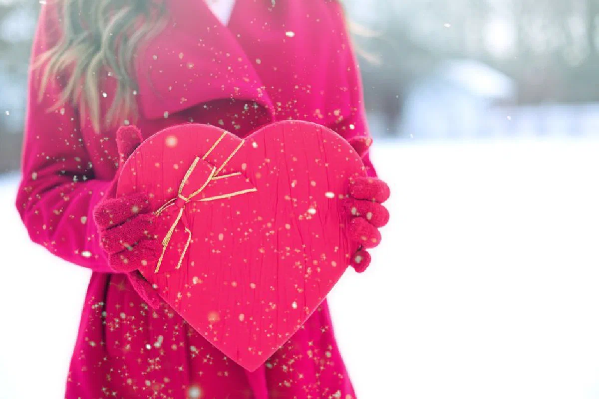 Woman in red holding a heart-shaped gift box in a snowy scene. Perfect for Valentine's themes.