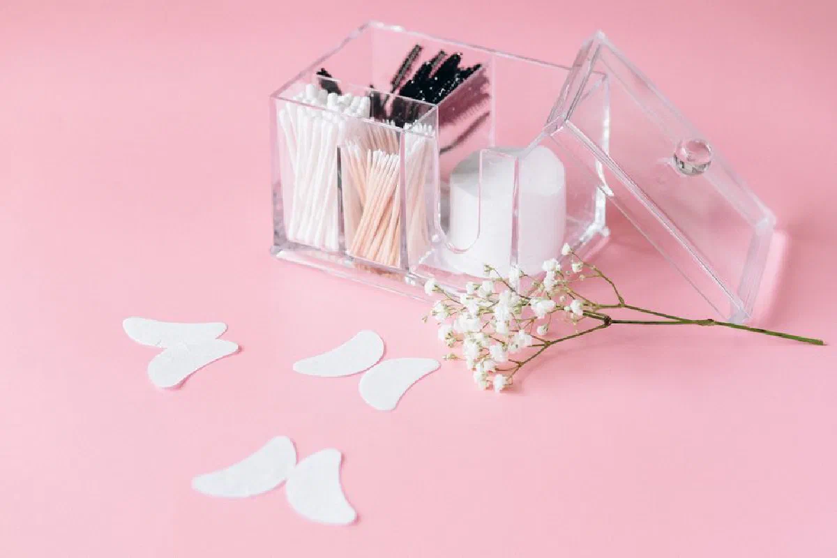 Clear makeup organizer with cotton swabs and brushes on a light pink background, with delicate baby's breath flowers.