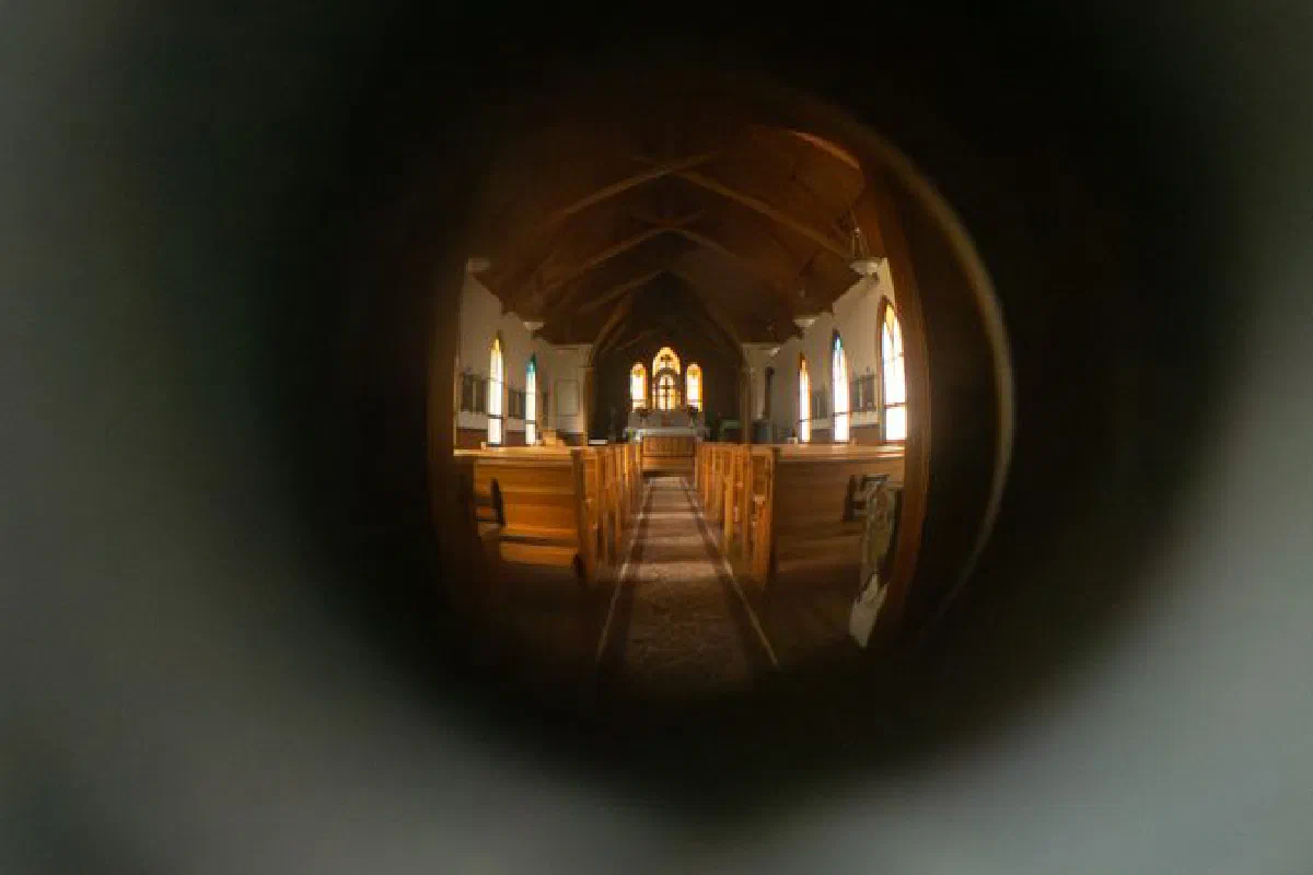 A unique keyhole perspective of a historic church interior in Silver City, Idaho, with wooden pews and stained glass windows.