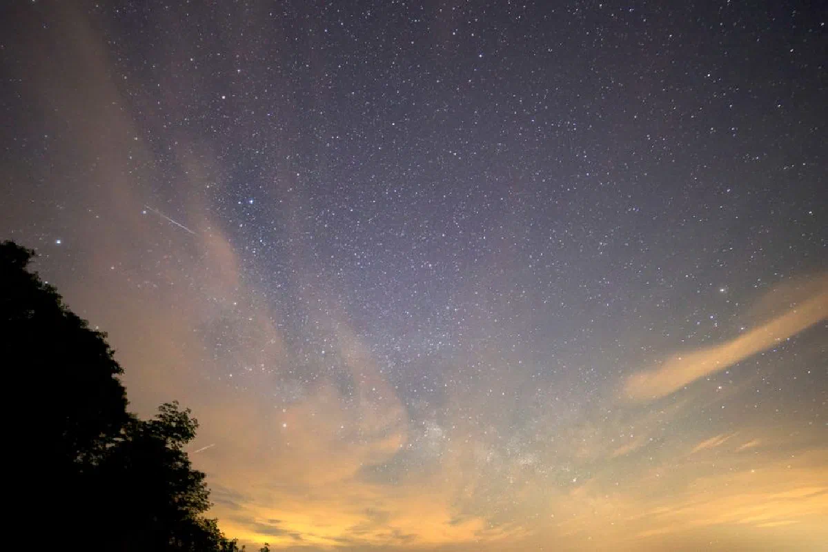 A breathtaking view of the star-filled night sky featuring the Milky Way and a meteor streak.