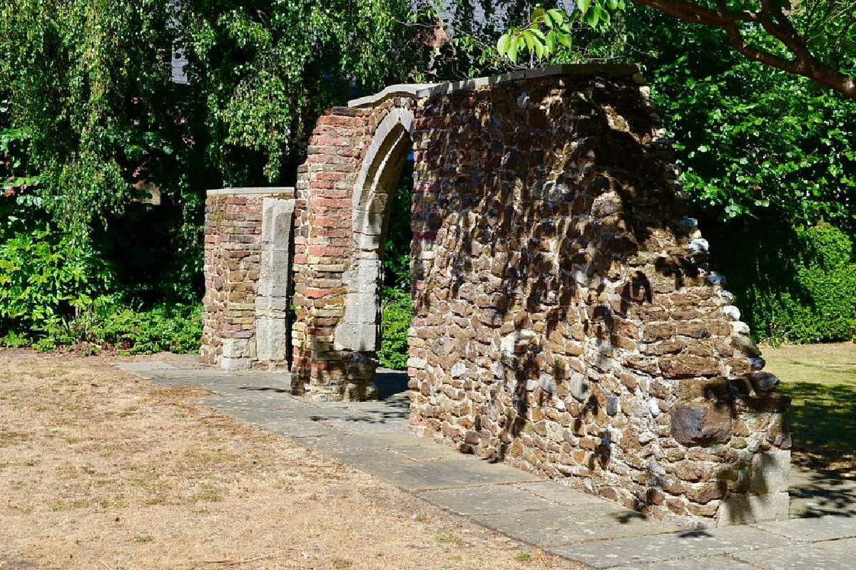 An old stone wall with archway in a sunlit garden, evoking history and rustic charm.