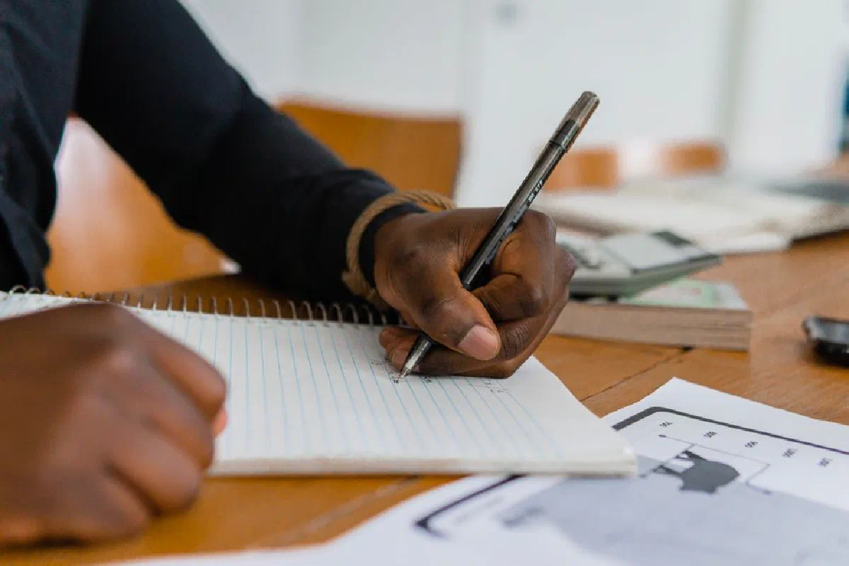 Close-up of hand writing on notebook at a wooden table, featuring paper and ballpen.