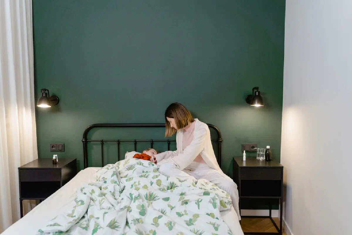 A mother cares for her child with a fever in a warm, cozy bedroom setting.