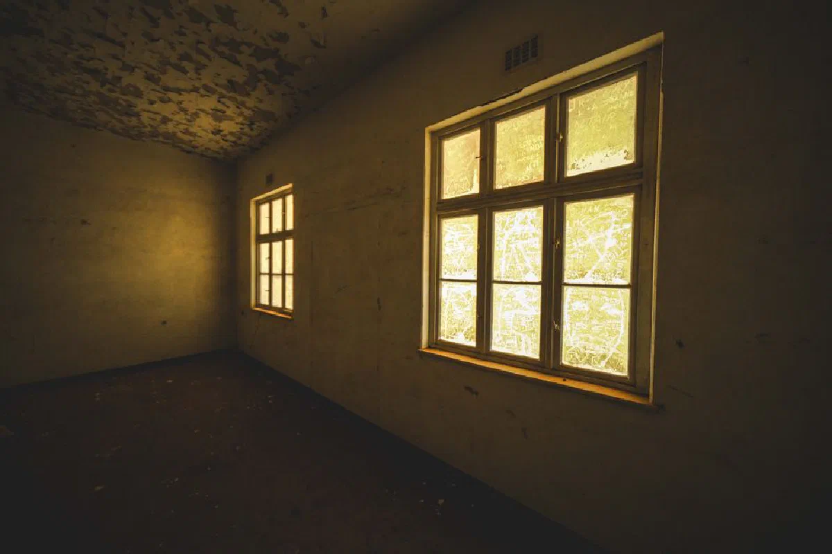 Empty abandoned room with sunlight streaming through dusty windows in Kolmanskop, Namibia.