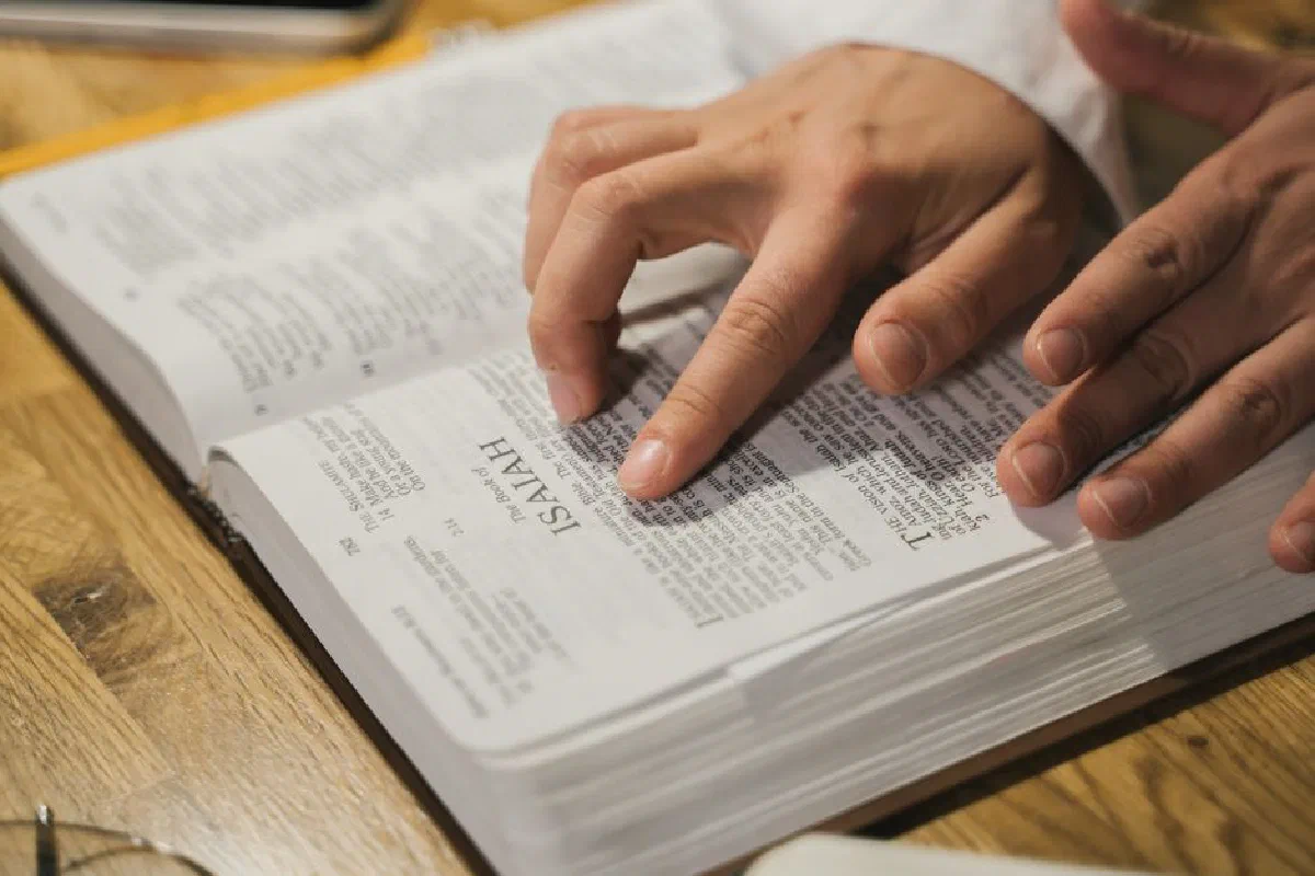 Close-up of hands reading a Bible, focusing on Isaiah passage, in an intimate indoor setting.