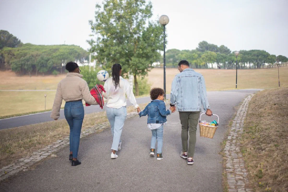 A family enjoys a peaceful walk in a picturesque park, holding hands and carrying a picnic basket.