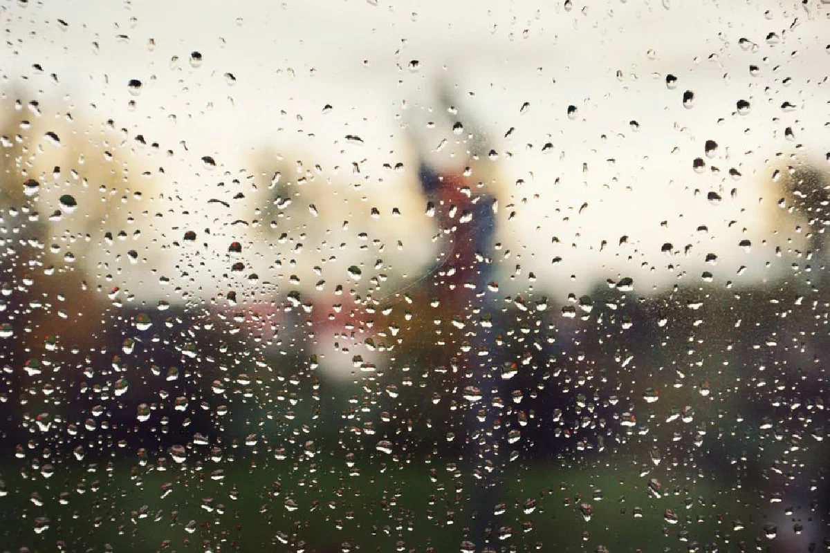 Rain droplets on glass with a blurred scenic background, creating a moody atmosphere.