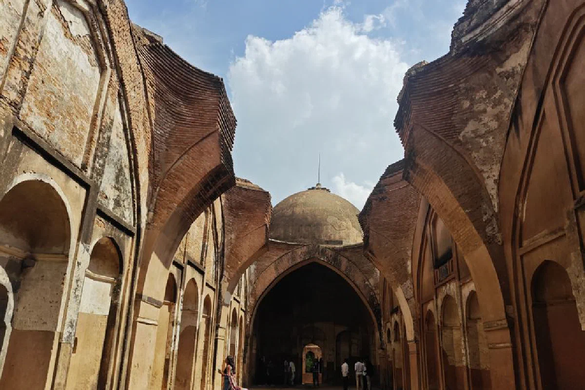 Historical arched corridor with a dome in Murshidabad, India, under a bright blue sky.