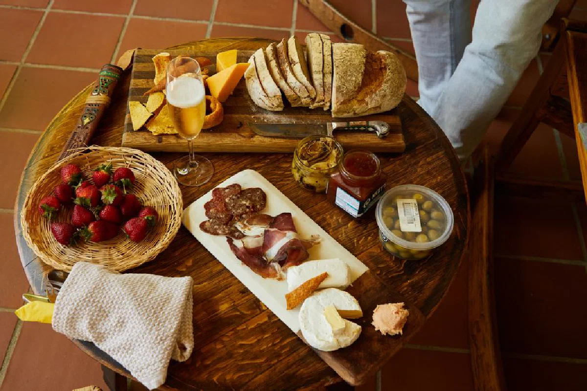A rustic charcuterie board with bread, cheese, strawberries, and a drink on a wooden table.