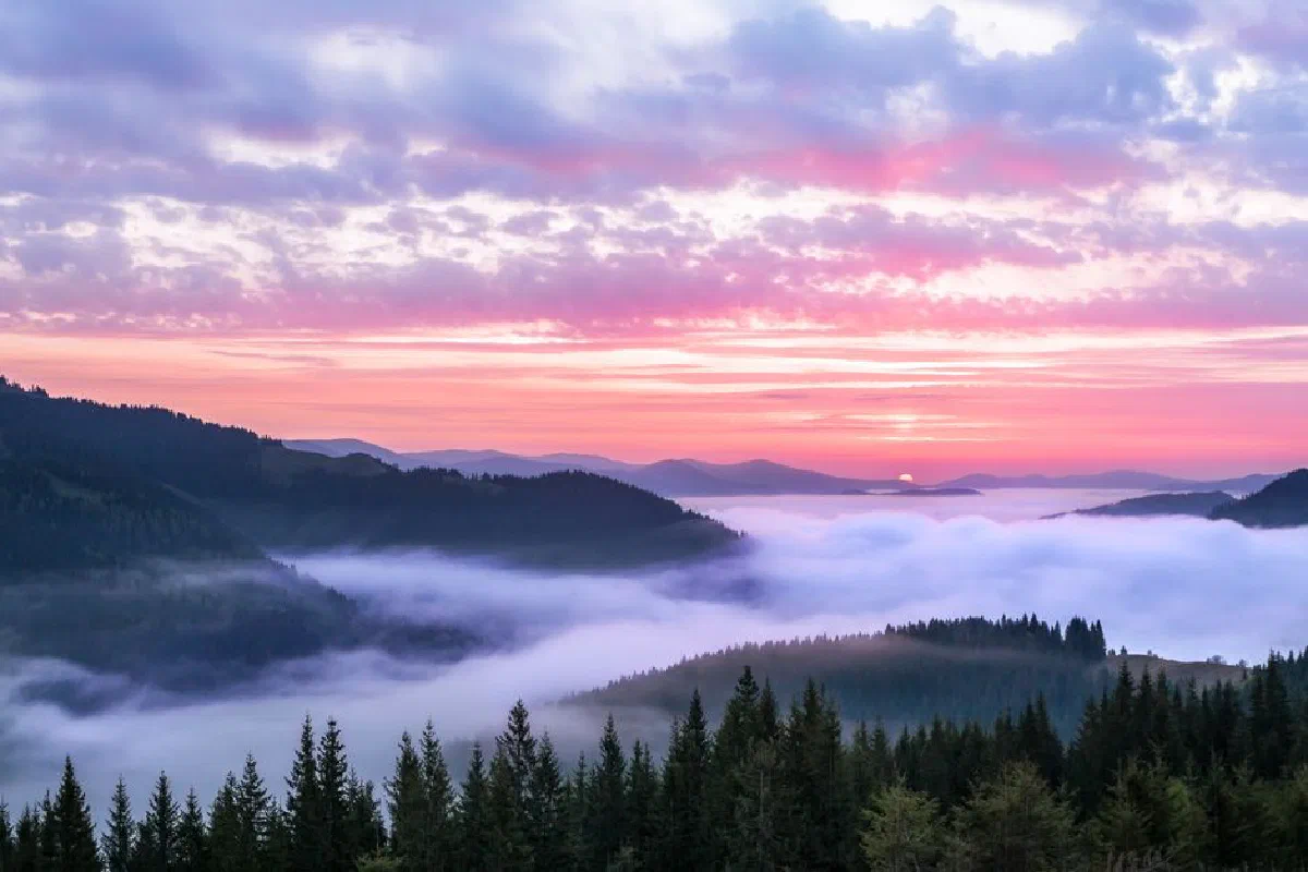Breathtaking view of a pink sunrise over a mist-covered mountain landscape with clouds.