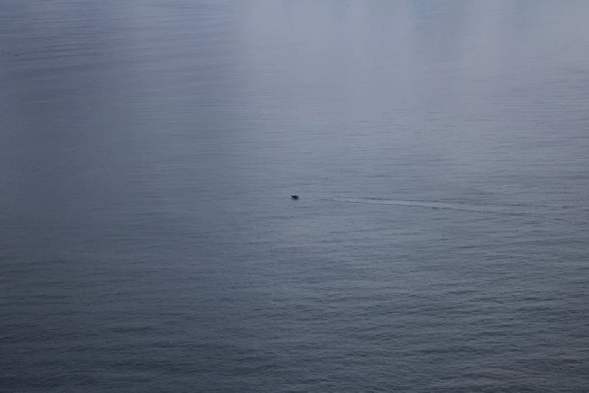 Minimalist seascape with a solitary boat on calm waters under a cloudy sky.