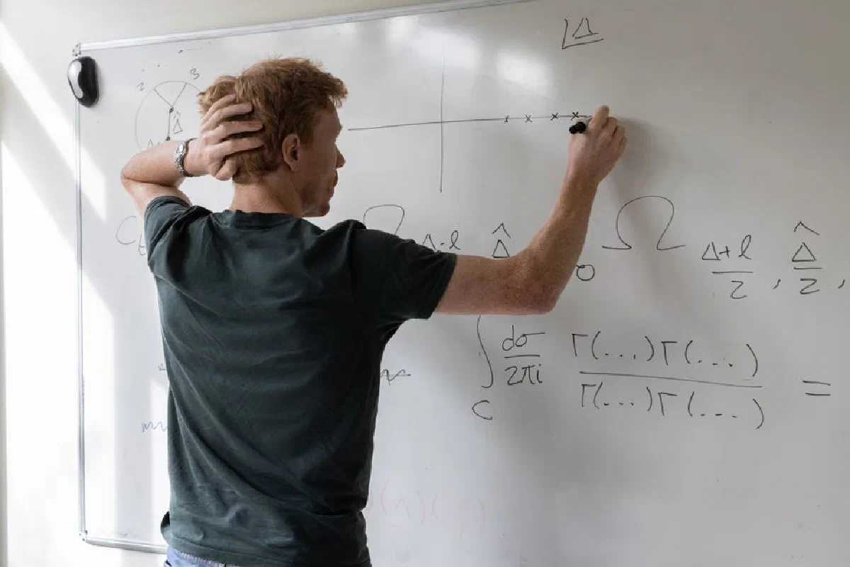 Teacher writing mathematical equations on whiteboard in a classroom setting.