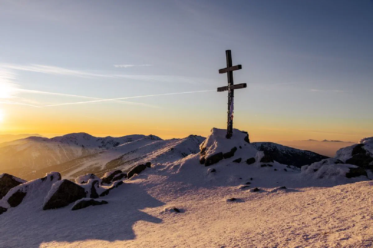 A stunning winter sunrise view of a cross on a snowy mountain peak in Slovakia.