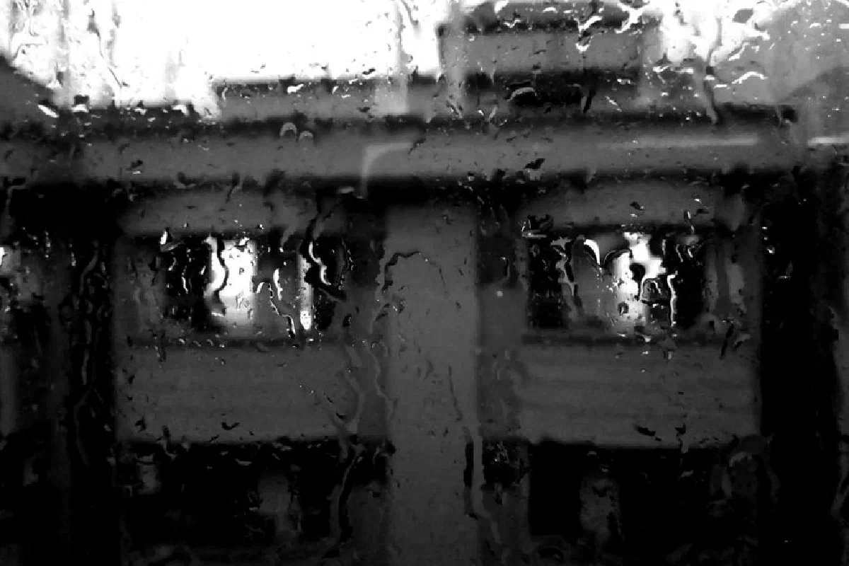 Black and white image of a building seen through rain-covered window in Dhaka.