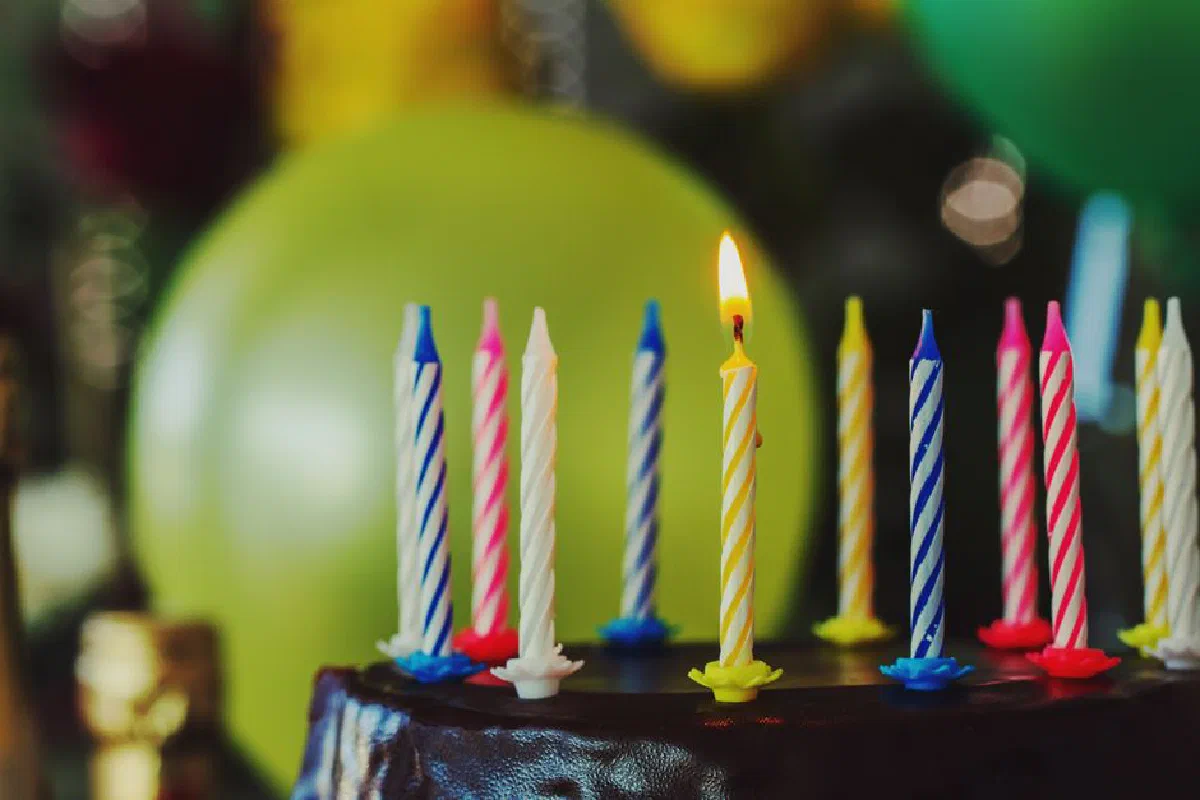 Colorful striped candles on a birthday cake with balloons in the background, perfect for party celebrations.