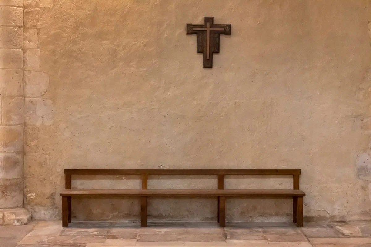 A tranquil church interior featuring a wooden pew and cross against a stone wall.
