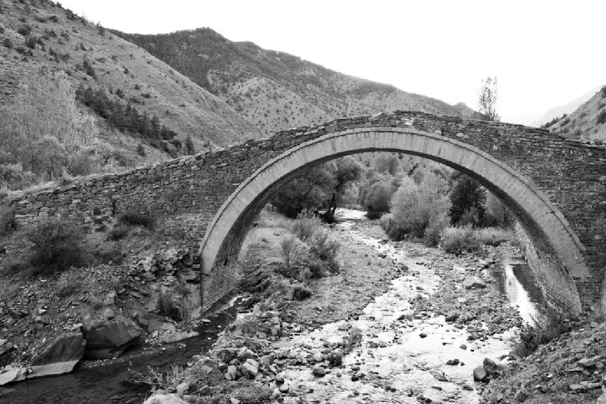 A scenic view of an ancient stone bridge arching over a flowing mountain stream.