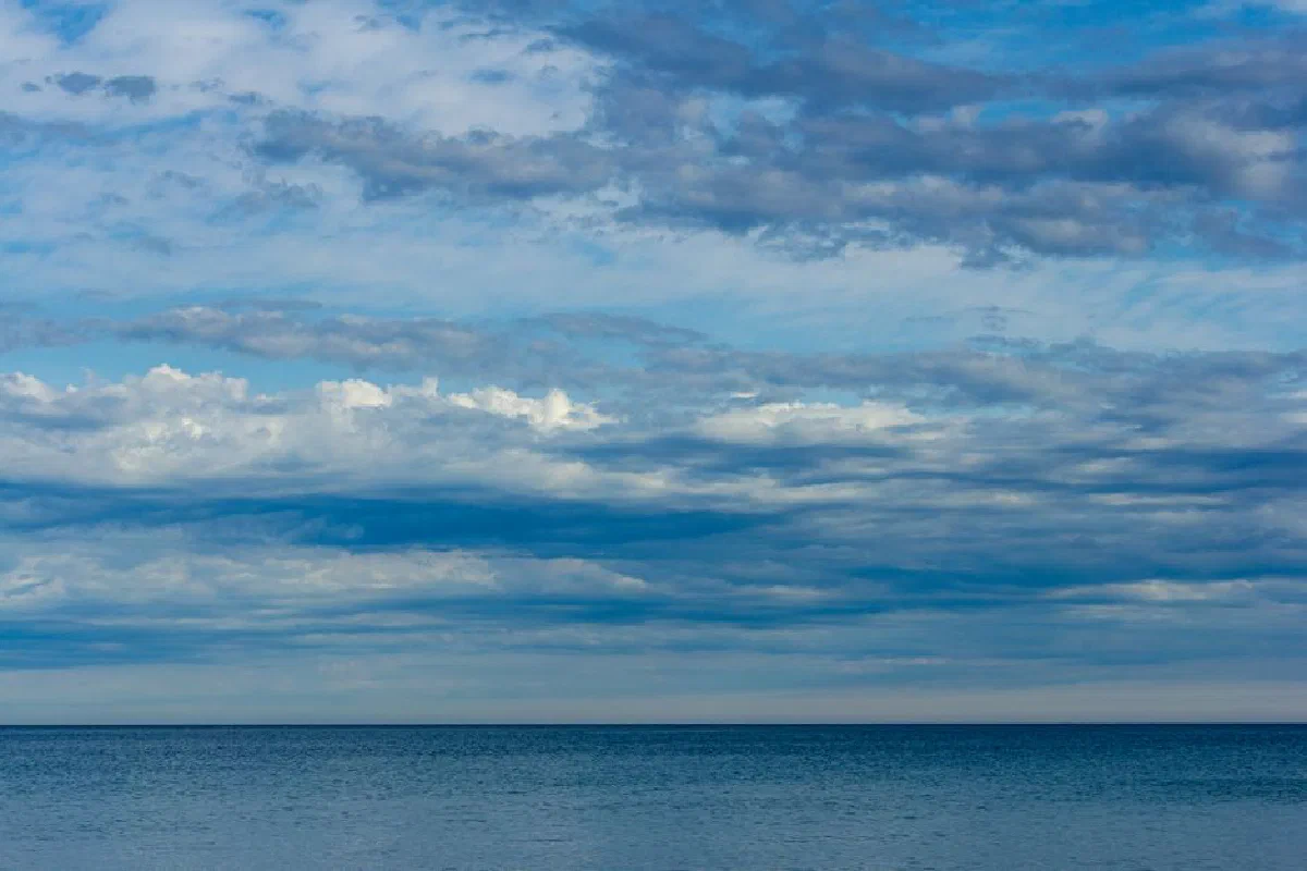 Capture the tranquility of a calm ocean beneath a vast and beautiful cloudy sky.