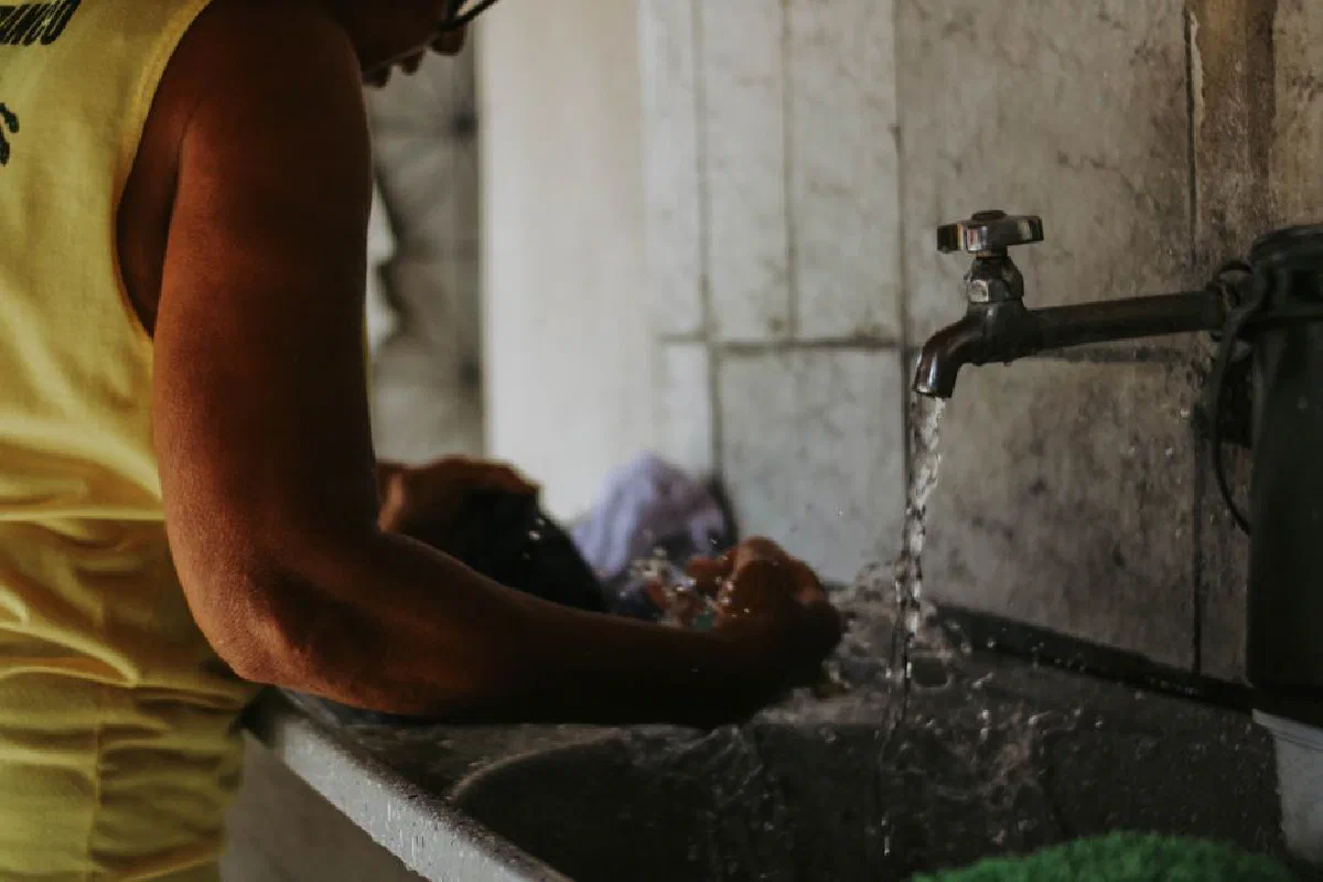 Close-up of a person washing clothes in a sink with running water indoors.