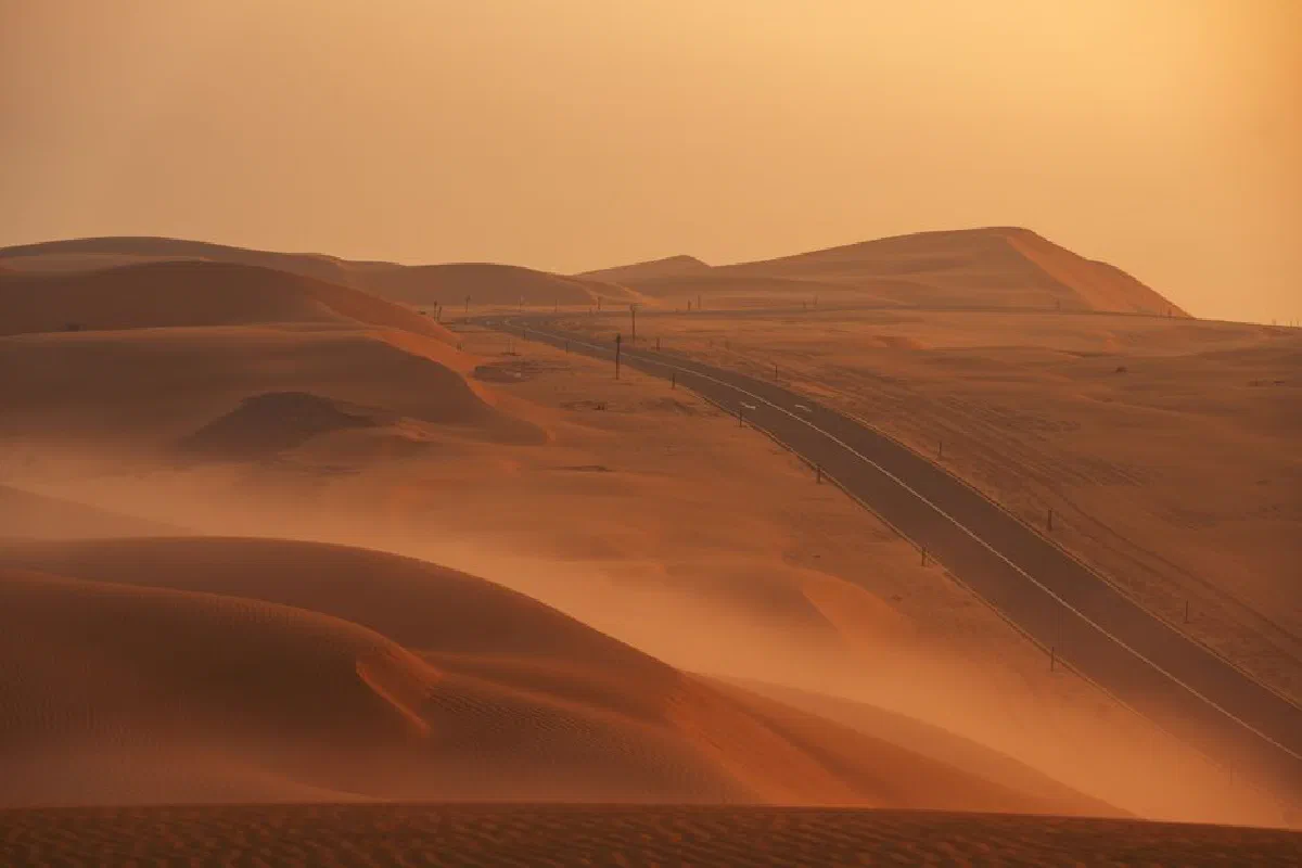 A scenic view of a highway cutting through vast desert sand dunes at sunset.