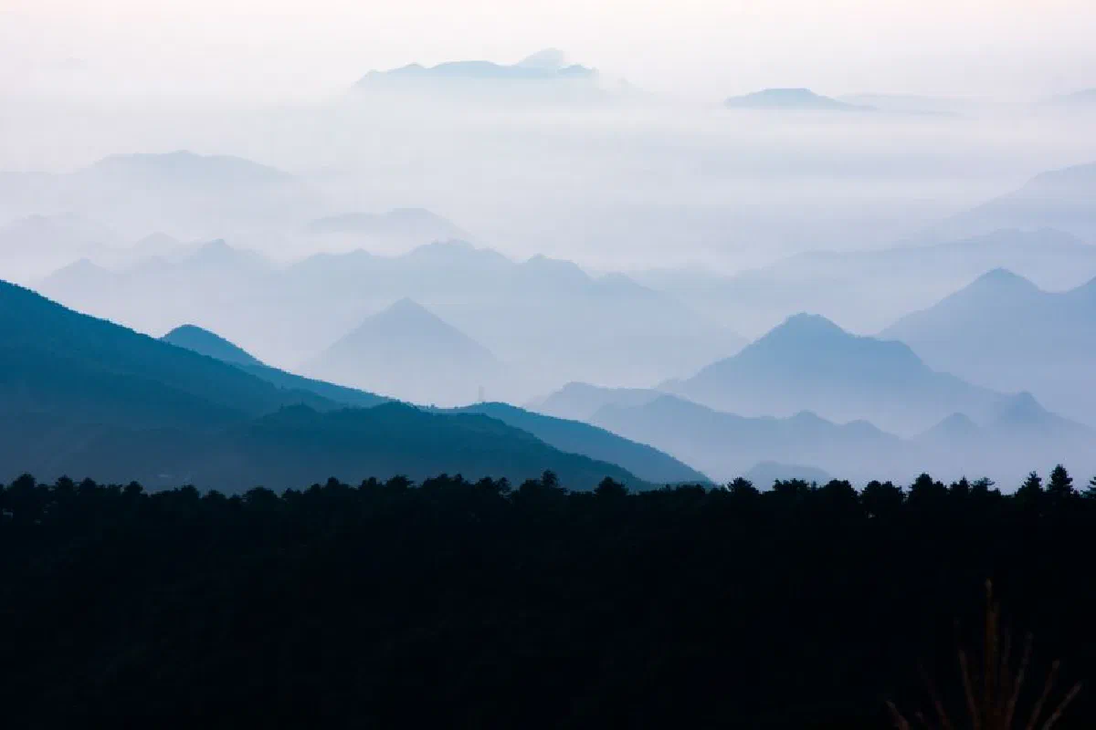 A serene view of layered mountains enveloped in mist, creating a mystical atmosphere.