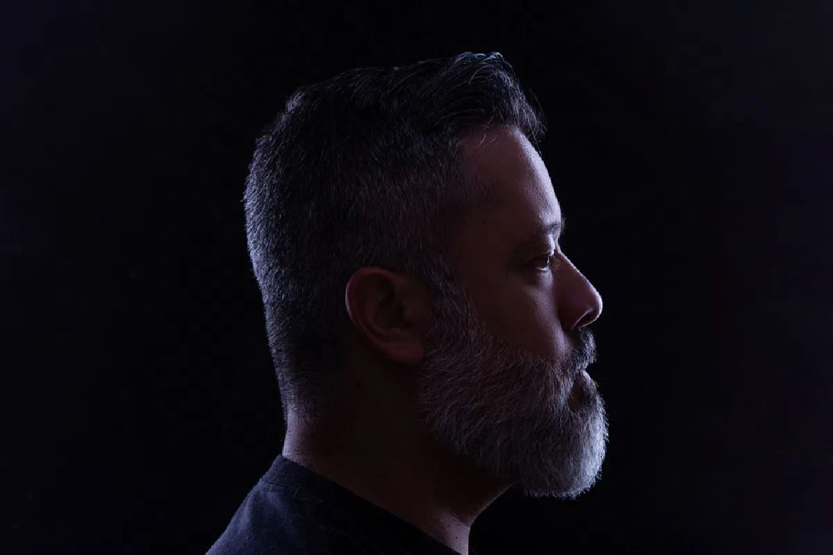 Side view portrait of a gray-haired man against a black background in a studio setting.